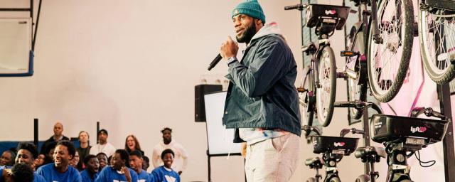 LeBron James in front of crowd of teenagers at a YMCA in New York, with a row of "Lyft" bikes behind him.