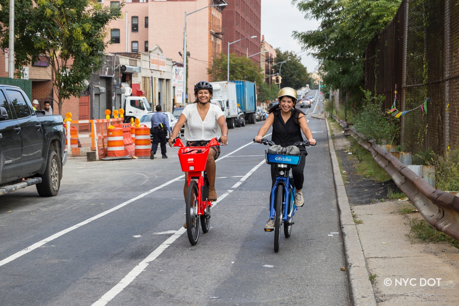 Two women riding dockless bike share in the Bronx. One is riding a red Jump bike, while the other is riding a blue Citi Bike. 