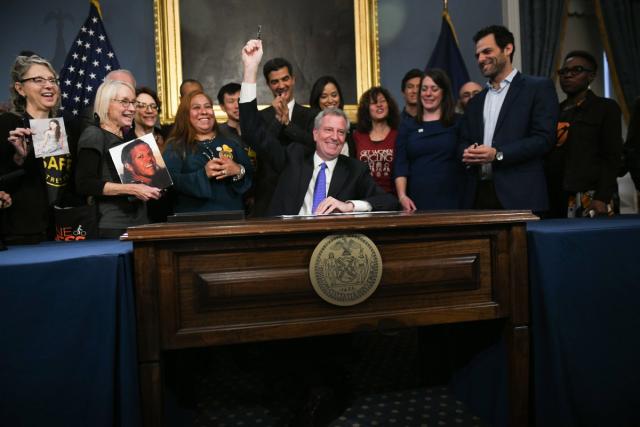 Mayor Bill De Blasio triumphantly raining his pen after signing the Safe Streets Bill. Surrounding him are members of "Families for Safe Streets", an advocacy group. 