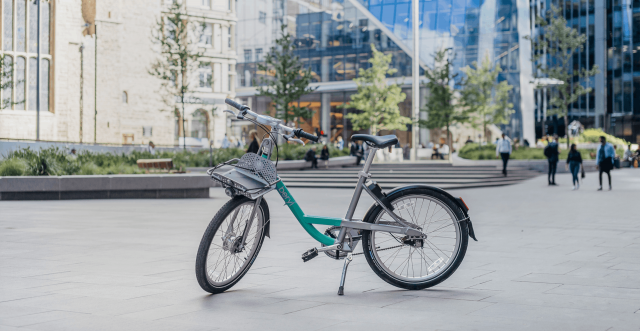 A photo of a Beryl bike in a plaza. It is a mint green and gray colored bike. 