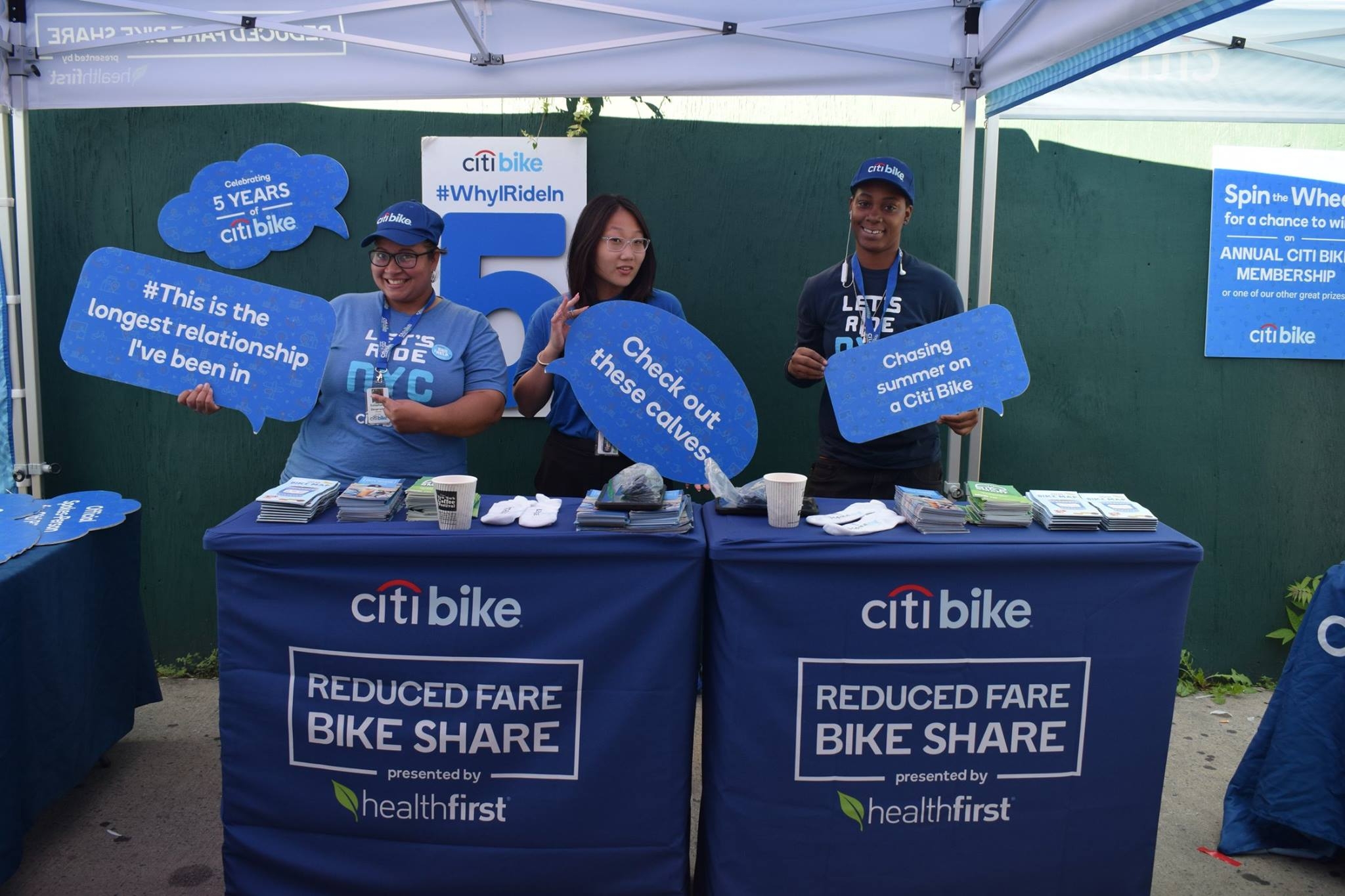 Citi Bike booth, with employees holding "speech bubbles" with phrases like "Check out these calves" and "Chasing summer on a Citi Bike". 