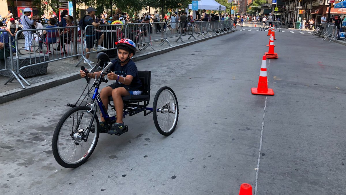 A young person using an adaptive handcycle. As opposed to a conventional bike, a handcycle has an upright seat close to the ground, with the pedals at roughly chest height. 