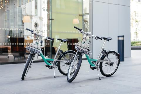 Two Beryl bikes, colored gray and sea green, in the middle of a city plaza